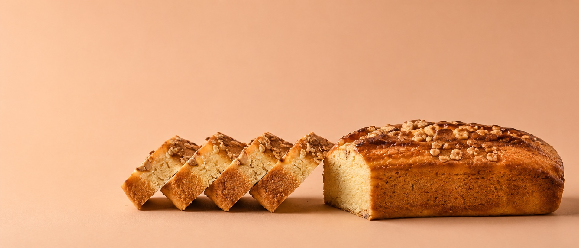 Walnut salted caramel loaf cake, part-sliced, on a warm blush background